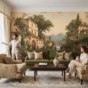 Op de afbeelding: Een woonkamer met een muurschildering van een Europees landschap, met een groene bank, fauteuils met patronen en een salontafel van donker hout. De kamer heeft een neutraal kleurenpalet met beige gordijnen en een vloerkleed met patroon. Een olijfboom in pot staat in de hoek.