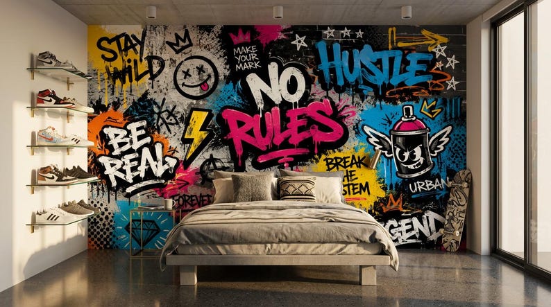May include: A bedroom featuring a wall mural with vibrant graffiti art, including the text "STAY WILD," "BE REAL," "NO RULES," "HUSTLE," and "BREAK THE SYSTEM." A bed with neutral bedding sits in front of the wall, with a skateboard and shelves of sneakers.