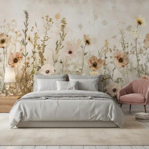 May include: A bedroom scene featuring a bed with light gray bedding, pillows, and a gray blanket. A floral mural in soft tones of beige, pink, and yellow adorns the wall behind the bed. A pink armchair and a wooden nightstand with a lamp complete the scene.