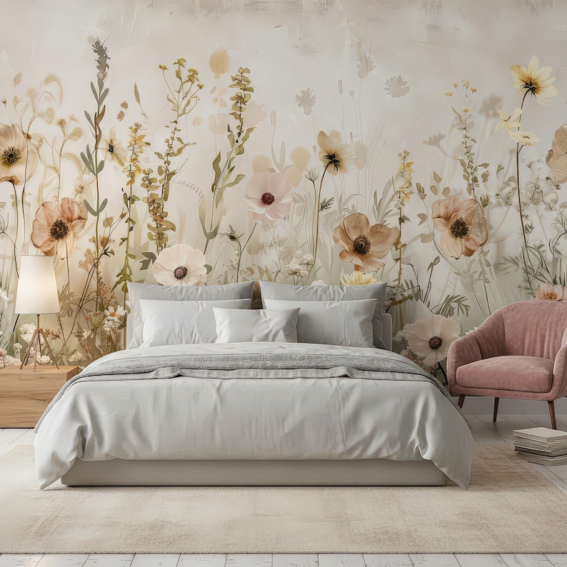 May include: A bedroom scene featuring a bed with light gray bedding, pillows, and a gray blanket. A floral mural in soft tones of beige, pink, and yellow adorns the wall behind the bed. A pink armchair and a wooden nightstand with a lamp complete the scene.