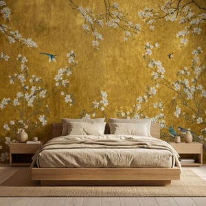 May include: A bedroom scene featuring a wooden bed frame with a beige comforter and pillows. The headboard is against a gold-colored wall adorned with a floral mural of white blossoms and blue birds. Two wooden nightstands flank the bed.