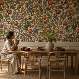 Può includere: Una sala da pranzo con carta da parati a motivo ripetuto di melograni e foglie verdi, un lungo tavolo in legno e diverse sedie in legno chiaro con schienali curvi. Un vaso in ceramica è posto sul tavolo accanto a ciotole scure.