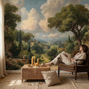 Op de afbeelding: Een serene scène met een muurschildering van een landschap en een persoon die in een stoel leest. Een rieten salontafel met kaarsen en een kleine keramische kan. De kamer heeft een vloerkleed en een raam met een gordijn.