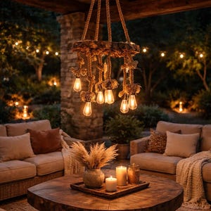 May include: A rustic outdoor living space featuring a wooden coffee table, beige sofas, and a unique chandelier made of rope and wood. The chandelier has several Edison-style light bulbs. The scene is illuminated by warm, inviting lighting.