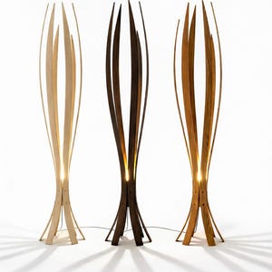 May include: Three wooden floor lamps in birch, walnut, and oak. Each lamp has a unique design with vertical wooden slats and a warm light emanating from within. The lamps are labelled with their wood type and the text "Easy and Simple to Assemble".
