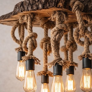 Peut inclure: Lustre rustique avec une base en bois brut et des bords naturels, suspendu par de grosses cordes. Il comprend six ampoules de style Edison avec des douilles noires, dégageant une lumière chaude. Luminaire unique et artisanal.