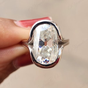 May include: A close-up of a silver ring with a large, rectangular, clear gemstone. The gemstone is the focal point, reflecting light and set in a smooth, polished silver band. The ring's design is elegant and modern, showcasing the brilliance of the stone.