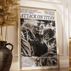 May include: A framed black and white Attack on Titan poster. The poster features manga-style illustrations of characters in action, with the title "ATTACK ON TITAN" prominently displayed. The frame is a light wood color.