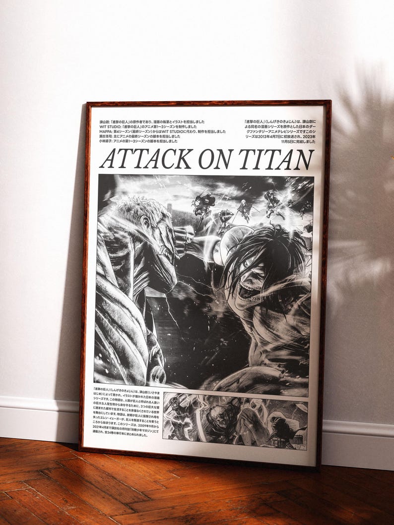 May include: Framed black and white Attack on Titan poster. The artwork features detailed illustrations of characters and action scenes from the anime series. The poster is displayed in a brown wooden frame, leaning against a white wall.