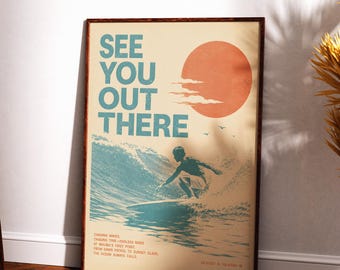 May include: A rectangular wall art print in a dark wood frame featuring a retro-style graphic of a surfer on a wave. The text reads "SEE YOU OUT THERE" in large blue letters, with a large orange sun, small birds, and additional text below.