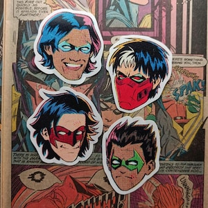 May include: Four stickers depicting comic book character faces with masks, set against a vintage comic book page. The stickers have white borders. The characters sport blue, red, and green masks and various hair colours.