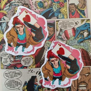 May include: Two die-cut stickers of Gambit from Marvel Comics, holding an Ace of Hearts playing card. The stickers have a pink outline and are set against a comic book panel background.