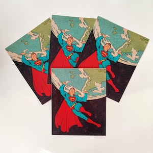 May include: Four vintage-style Superman art prints. Each print features Superman in a blue suit with a red cape, lifting the Earth. The background is a dark space with a light-colored planet.