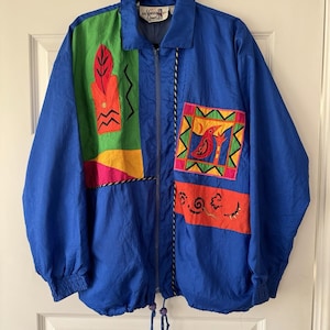 以下が含まれることがあります： カラフルな幾何学模様のパッチが付いた、ヴィンテージの青いジャケット。 ジャケットはフルジッパー、襟、伸縮性のある袖口が特徴です。 パッチには、赤い鳥、葉、緑、黄、オレンジ、ピンクの抽象的なデザインが含まれています。
