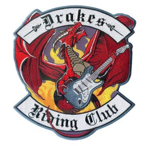 May include: An embroidered patch featuring a red dragon playing a grey electric guitar against a yellow and purple flame background. The design includes white banners with black text reading Drakes at the top and Riding Club at the bottom.