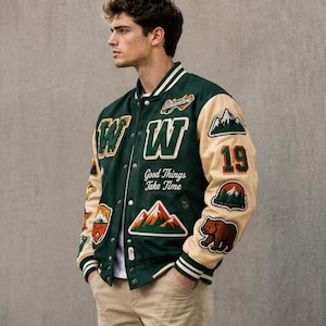 May include: A dark green varsity jacket with cream-colored sleeves, featuring embroidered patches of mountains, a bear, and the number 19. The front displays the letter W, the text Good Things Take Time, and striped ribbed trim on the collar and cuffs.