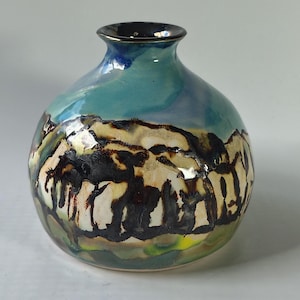 May include: A round ceramic vase with a narrow neck and a glossy finish. The surface features a hand-painted design with a vibrant blue upper section and a lower section decorated with abstract black, cream, and yellow brushstroke patterns.
