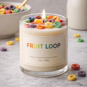 Puede incluir: Vela encendida en vaso transparente con base de cera blanca, adornada con cereales de colores. La vela tiene una etiqueta que dice "FRUIT LOOP". La vela pesa 340g.