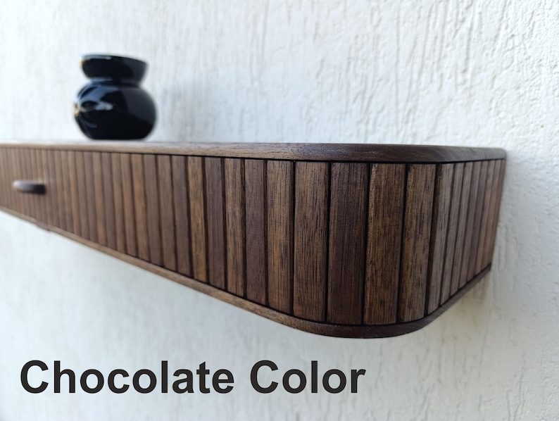 以下が含まれることがあります： チョコレート色の木製フローティングシェルフ。引き出しと小さな丸い黒い花瓶が付いています。シェルフは溝のある垂直デザインです。「Chocolate Color」の文字が画像の下部にあります。
