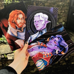 Könnte beinhalten: Drei Kunstdrucke mit Fantasy-Charakteren. Ein Druck zeigt einen rothaarigen Charakter mit einem Pelzkragen. Ein anderer zeigt einen Charakter mit weißen Haaren und spitzen Ohren. Der dritte Druck zeigt einen lila Charakter mit Hörnern.