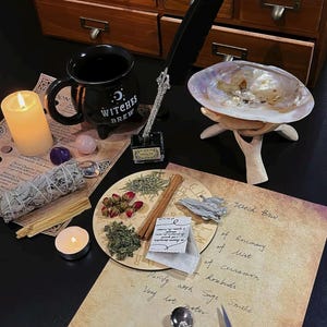 May include: A still life arrangement featuring a black mug with "Witches Brew" text, a feather quill, a seashell, and various herbs and spices. A lit candle and handwritten notes are also present, creating a mystical theme.