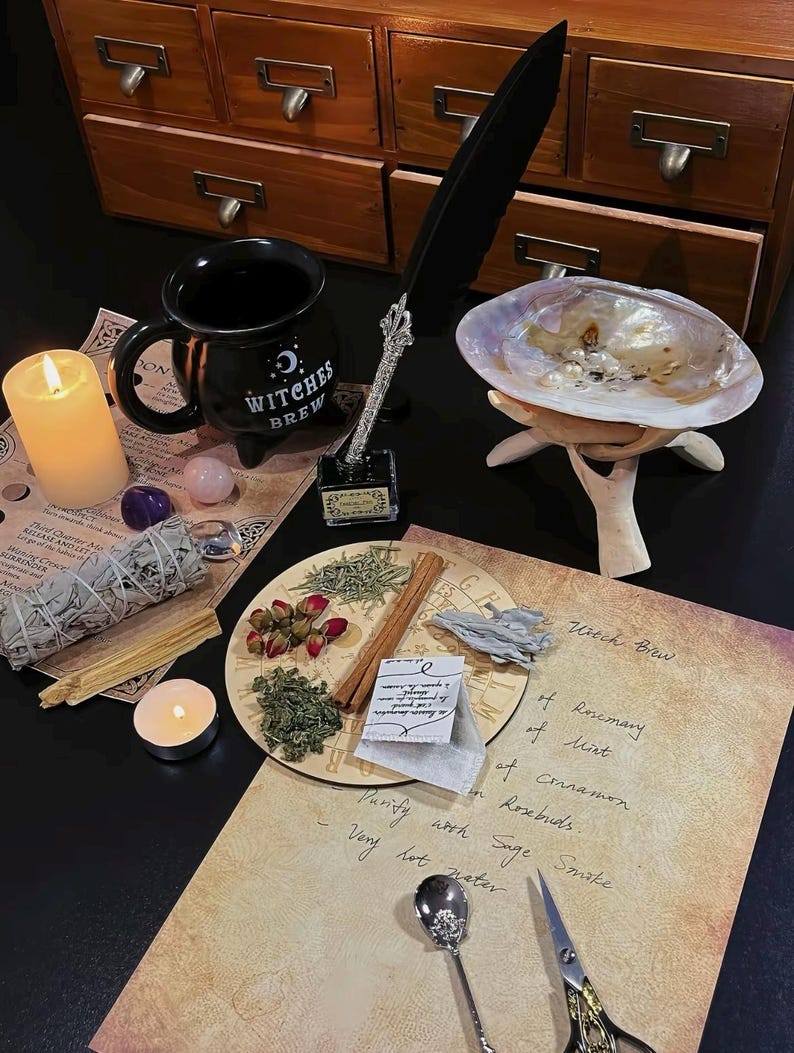 May include: A still life arrangement featuring a black mug with "Witches Brew" text, a feather quill, a seashell, and various herbs and spices. A lit candle and handwritten notes are also present, creating a mystical theme.