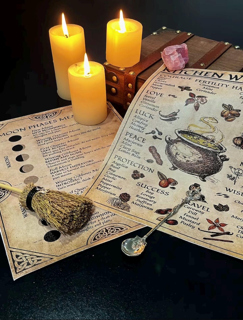 May include: Three lit yellow candles next to a wooden chest and printed papers with text and illustrations. A small broom and a decorative spoon are also present. The papers feature text about moon phases and kitchen witchery.