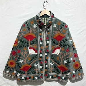 Könnte beinhalten: Salbeigrüner Jacke mit aufwendiger Blumenstickerei in Rot, Orange, Weiß und Braun. Die Jacke hat einen hohen Kragen und einen Reißverschluss. Die Stickerei zeigt stilisierte Blumen und Blätter mit Mustern an den Kanten und Ärmeln.