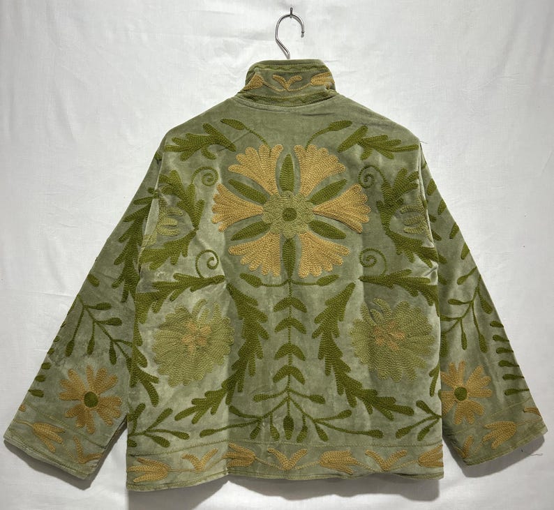 May include: A light green jacket with long sleeves and a high collar. The jacket is adorned with intricate floral embroidery in shades of gold and green. The embroidery is centered on the back and sleeves.