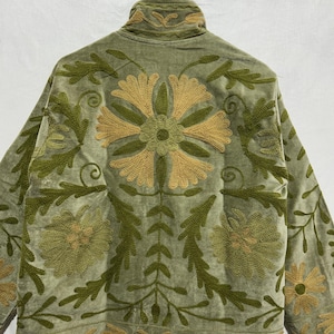 May include: Sage green jacket with intricate floral embroidery in shades of olive and gold. The jacket features a high collar and long sleeves, with detailed patterns on the back and sleeves. The fabric appears to be a soft velvet.