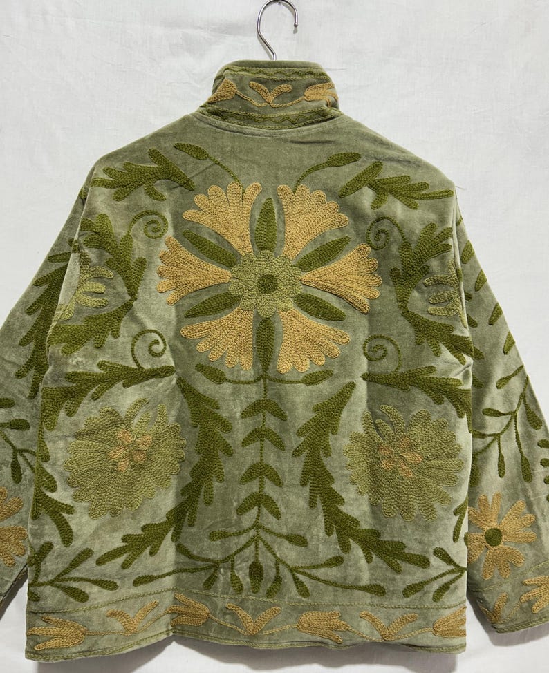 May include: Sage green jacket with intricate floral embroidery in shades of olive and gold. The jacket features a high collar and long sleeves, with detailed patterns on the back and sleeves. The fabric appears to be a soft velvet.