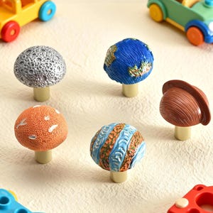 May include: A collection of decorative mushroom-shaped cabinet knobs. The knobs feature various designs, including a moon, Earth, and other patterned surfaces. The knobs are in various colors, including silver, blue, orange, and brown.