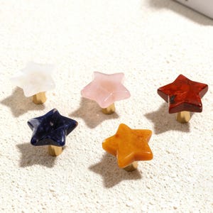 May include: Five star-shaped cabinet knobs in various colours: white, pink, red, blue, and orange. Each knob is made of polished stone and has a gold-coloured base. These decorative knobs are ideal for adding a unique touch to furniture.