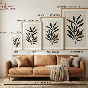 May include: Four framed botanical art prints of varying sizes, featuring black leaf designs on a beige background, are displayed above a brown leather sofa. The largest print measures 47.24" x 70.87". The room is decorated with neutral tones.