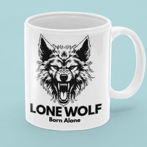 May include: White ceramic mug featuring a black and white illustration of a snarling wolf's head. The text "LONE WOLF" is printed below the image, with "Born Alone" underneath. The mug has a white handle.