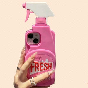 May include: A pink phone case shaped like a spray bottle, with a white trigger and the word "FRESH" in red letters. The case has a round label with the word "monday" on it.