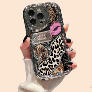 May include: A decorative phone case with a silver frame and a collage of patterns. The case features a leopard print, zebra stripes, a pink glitter lip design, and the text "Who's that GIRL?"