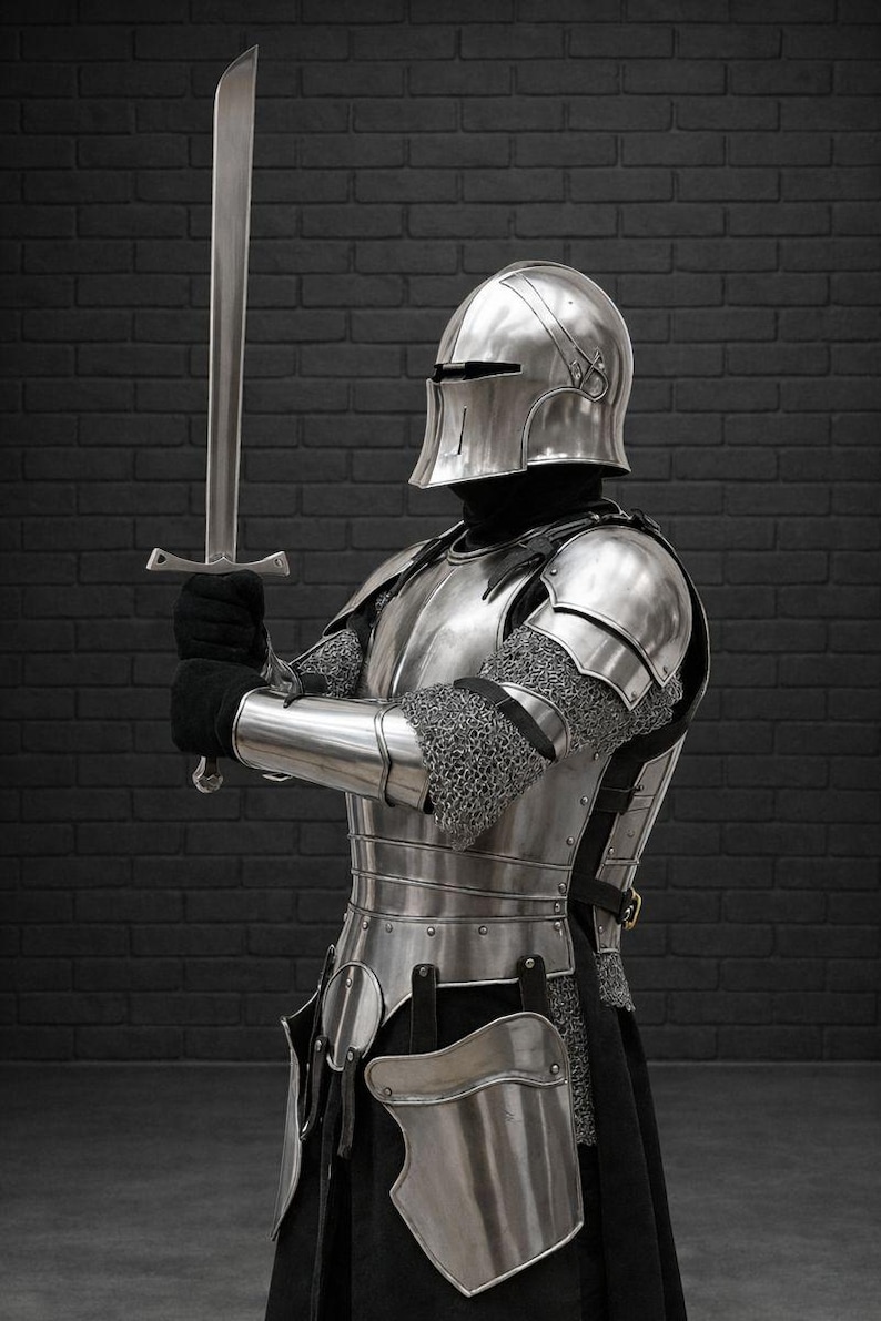 May include: A full suit of medieval armor, including a helmet, chest plate, and leg guards, is displayed. The silver-colored armor is worn over a black garment. The knight holds a long, silver sword in a defensive stance.