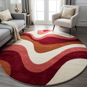 Könnte beinhalten: Ein runder Teppich mit einem wellenförmigen Muster in Rot-, Orange- und Cremetönen. Das Design des Teppichs weist fließende Linien und ein weiches, strukturiertes Aussehen auf, das für ein Wohn- oder Schlafzimmer geeignet ist. Der Teppich ist ein dekorativer Bodenbelag.