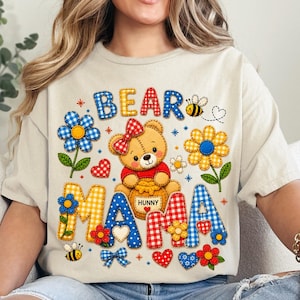 Könnte beinhalten: Beiges T-Shirt mit einem farbenfrohen "Bear Mama"-Motiv. Das Design zeigt einen Teddybären, der einen Honigtopf hält, umgeben von Blumen, Herzen und Bienen. Die Buchstaben sind im Patchwork-Stil mit verschiedenen Mustern.