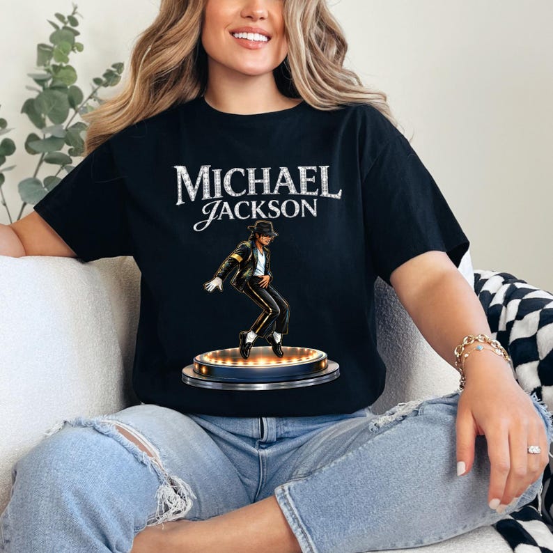 May include: Black t-shirt featuring the name "MICHAEL JACKSON" in white, with a graphic of Michael Jackson in a black suit and hat. The graphic is on a circular stage with lights.