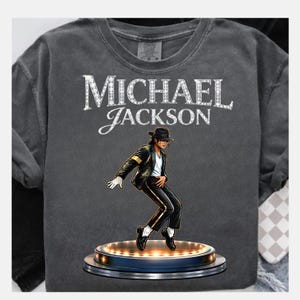 May include: Dark gray t-shirt featuring the text "MICHAEL JACKSON" in white, with a stylized image of Michael Jackson in a black suit and hat, performing on a stage with lights.