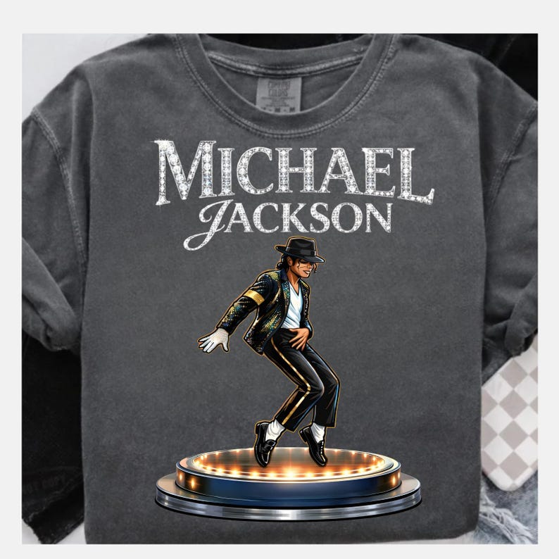 May include: Dark gray t-shirt featuring the text "MICHAEL JACKSON" in white, with a stylized image of Michael Jackson in a black suit and hat, performing on a stage with lights.