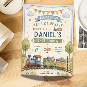 May include: A rectangular birthday invitation card featuring a watercolor train theme. The text reads ALL ABOARD! LET'S CELEBRATE DANIEL'S 2ND BIRTHDAY! SATURDAY MAY 17 AT 2:00 PM THE STATION 1213 RAILROAD LANE AUSTIN, TEXAS 78701 RSVP TO MIA AT 123.456.7890.