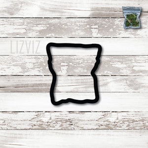 May include: Black cookie cutter shaped like a bag with a wavy top and bottom. The cookie cutter is on a white wood background.