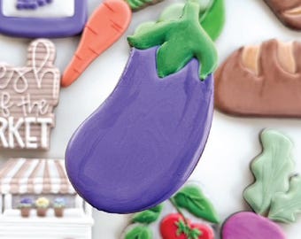 May include: Assortment of decorated cookies in the shape of various vegetables and market items. Includes a purple eggplant, carrot, tomatoes, and a jar of jam. Other cookies include a loaf of bread and a market cart.