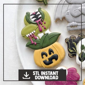 May include: A decorated sugar cookie shaped like a yellow pumpkin with a black jack-o'-lantern face, topped with dark green leaves and two light green carnivorous plants featuring white teeth and dripping pink icing accents on a white plate.