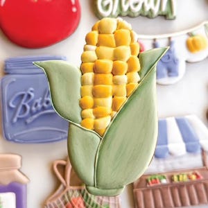 May include: A selection of decorated biscuits shaped like fresh produce and related items. The image shows a corn on the cob, a red tomato, a jar, and a sign that says "Locally Grown". Other biscuits include a farmer's market and a shopping bag.