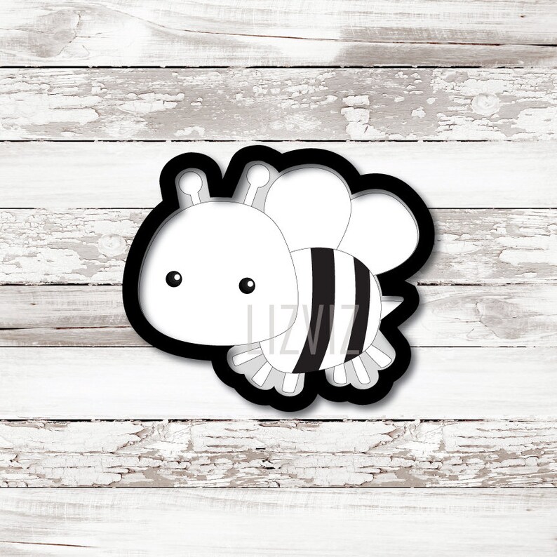 May include: Black and white cookie cutter in the shape of a cartoon bee. The bee has a round head with two small eyes and two antennae. The body is striped black and white.