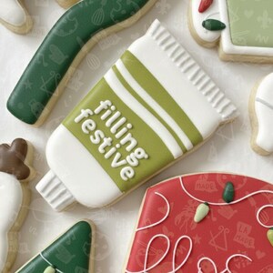 May include: A selection of decorated biscuits. One biscuit is shaped like a white tube with green stripes and the words "filling festive". Other biscuits are green, red, and white, with various shapes and designs.